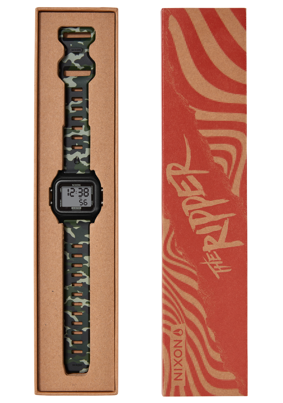 A Nixon "The Ripper" digital watch with a camouflage band is displayed in an open brown cardboard box next to its red and tan patterned sleeve. View 10