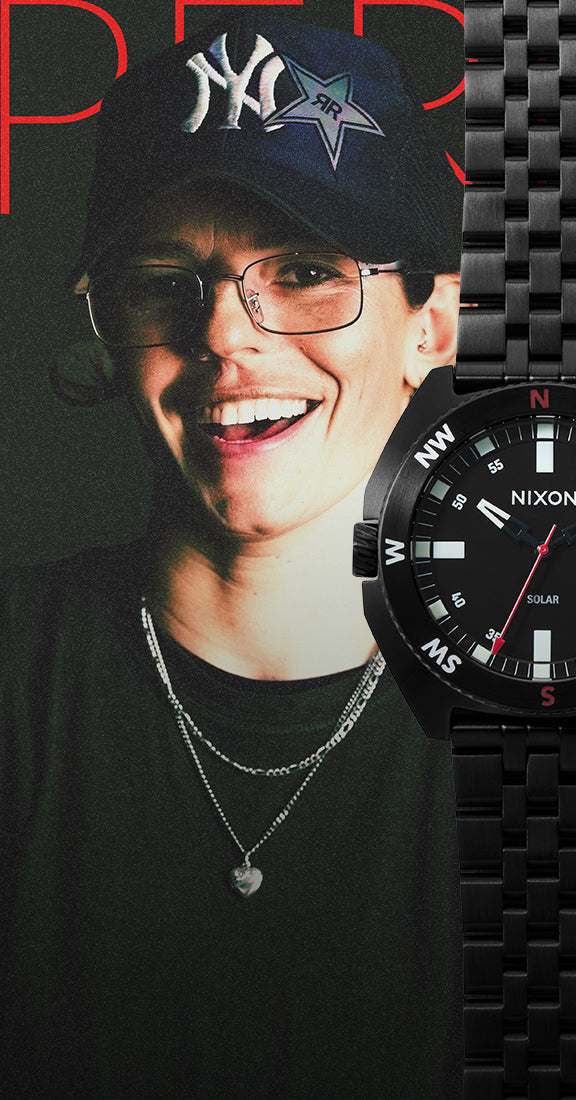 A person wearing a black NY Yankees cap, glasses, layered silver necklaces, and a black Nixon Solar watch with a black metal bracelet, set against a dark background with red lettering.